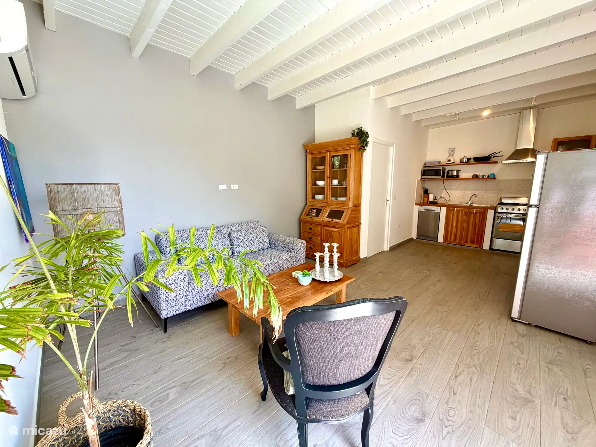 Ruime, lichte en gezellig ingerichte woonkamer met open keuken. De woonkamer heeft een airco en grote openslaande deuren. In de keuken staat een grote koelkast met vriezer.