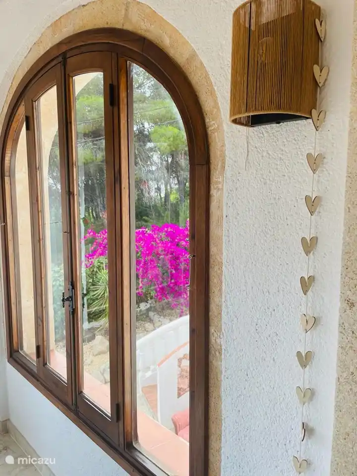 Im Garten blüht eine schöne Bougainvillea. Das Haus hat große Fenster, die es im Wohnzimmer sehr hell machen