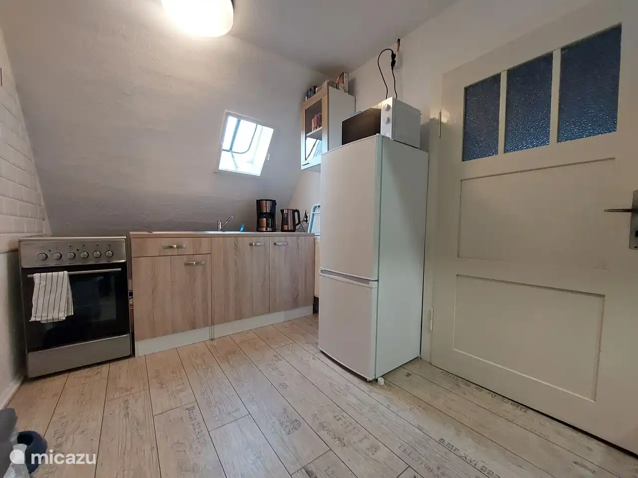 The cozy kitchen with ceramic stove with electric oven, microwave, refrigerator, coffee maker, kettle, toaster and sandwich maker.