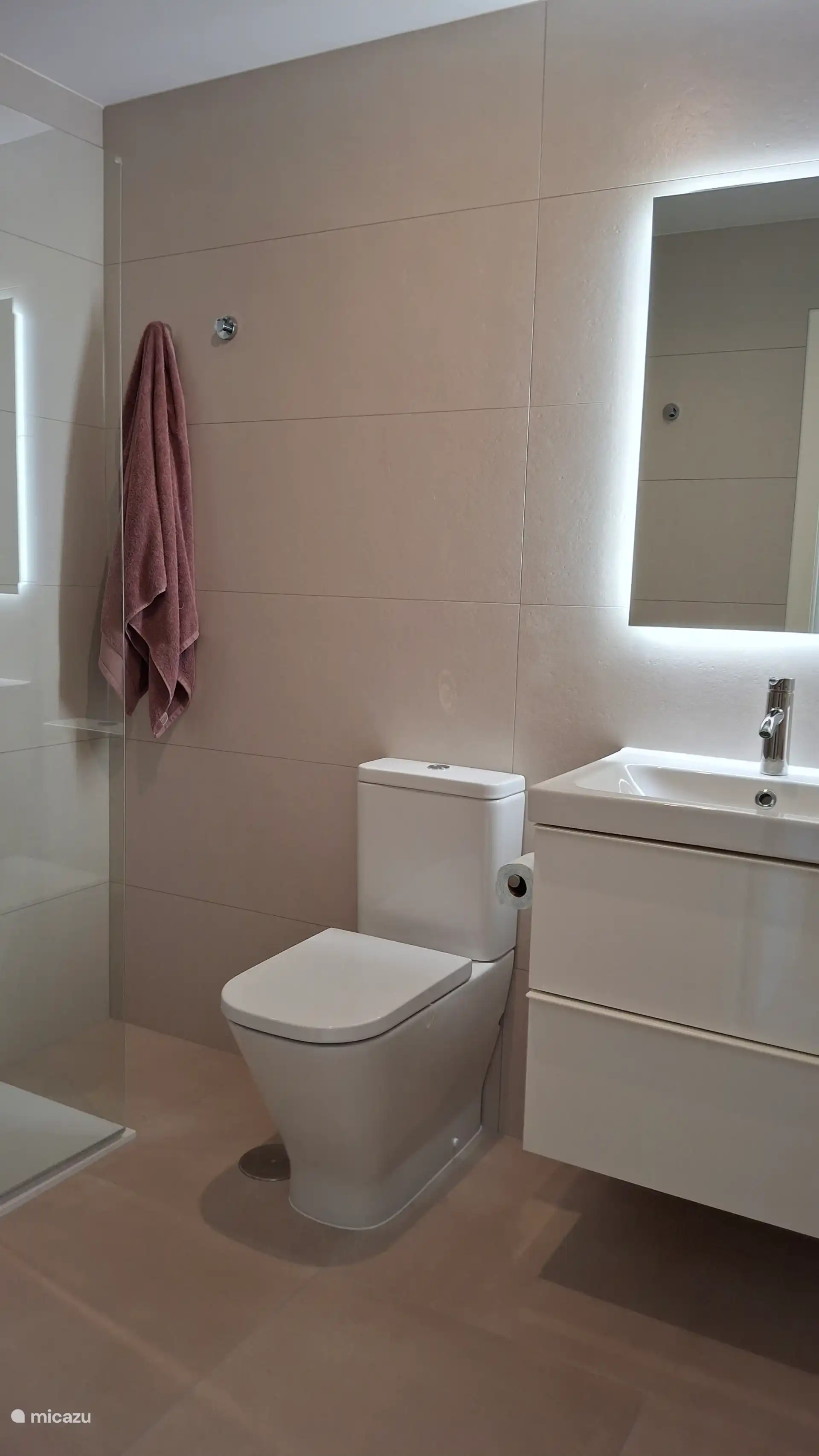 Luxuriöses Badezimmer mit Waschbecken, Spiegel, hoher Toilette, begehbarer Dusche und Föhn.