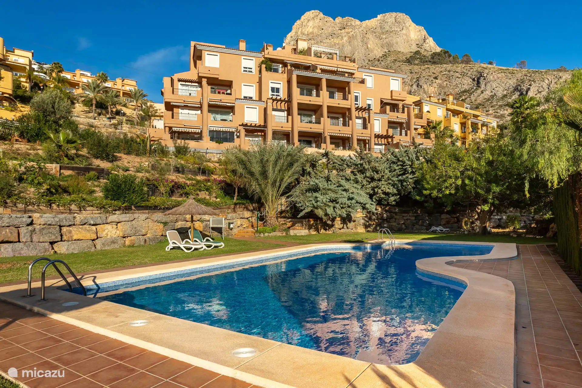 Dit is het tweede zwembad en ligt lager in de tuin. Hier kun je een ligbedje pakken. Er zijn parasols en er is een douche.