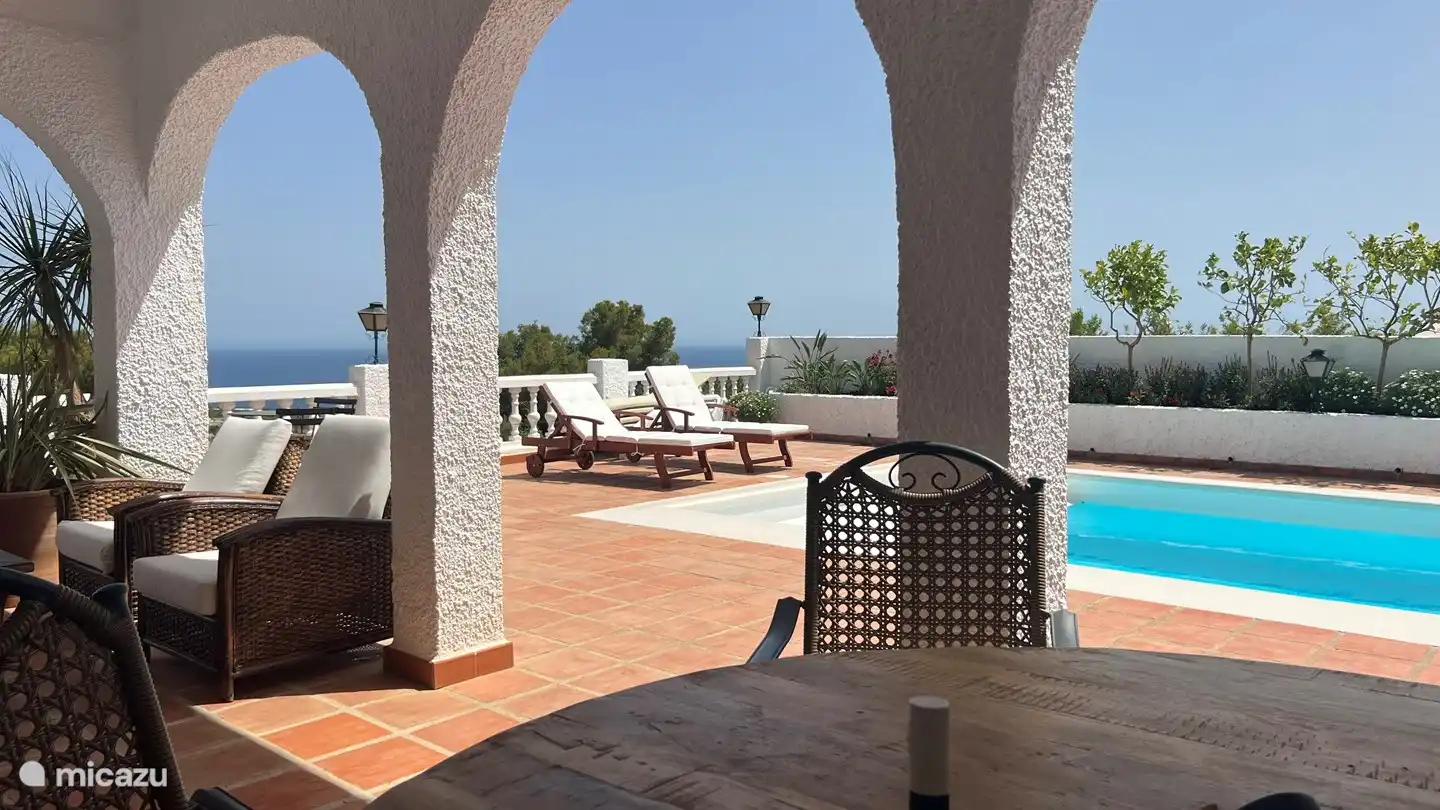 Genießen Sie ein Essen im Freien am großen Esstisch mit Blick auf den Garten mit Pool und das Meer