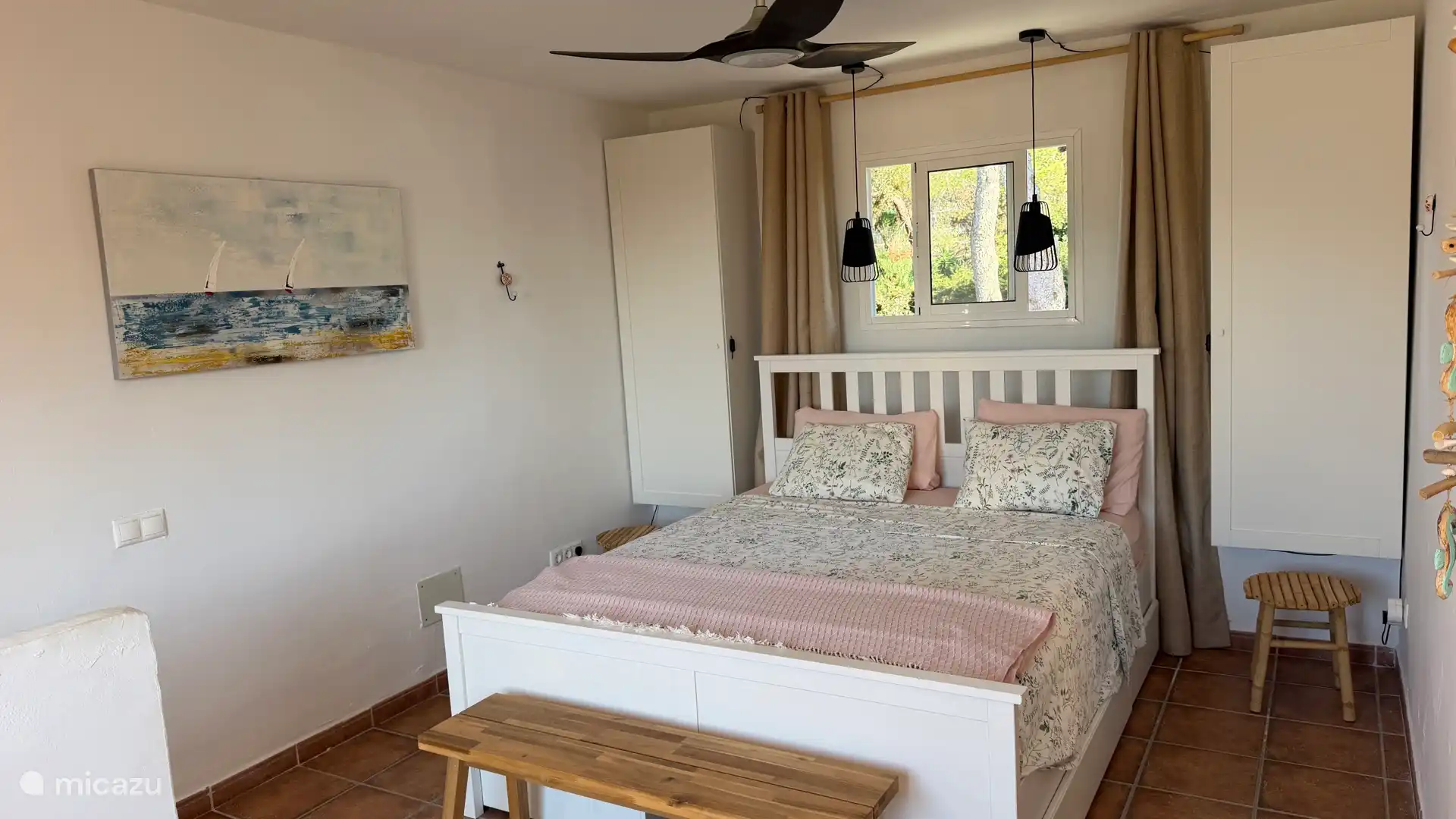 Slaapkamer met tweepersoonsbed met topper en plafondventilator.