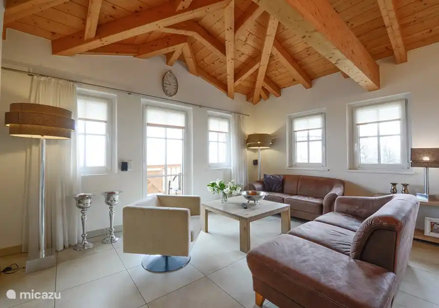 The beautiful spacious living room with high wooden ceiling, modern furnishings, lots of light and a beautiful view over Kaprun. You have direct access to the balcony, there is a large dining table, kitchen and a fireplace to enjoy and cozy.