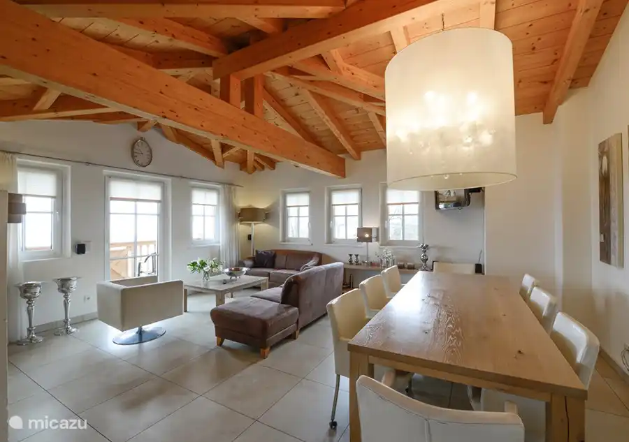 The beautiful spacious living room with high wooden ceiling, modern furnishings, lots of light and a beautiful view over Kaprun. You have direct access to the balcony, there is a large dining table, kitchen and a fireplace to enjoy and cozy.