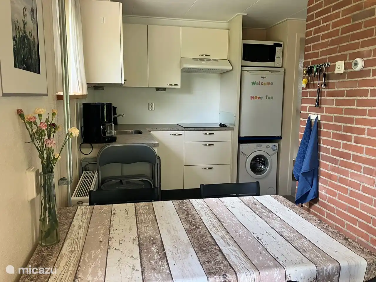 Open keuken met vaatwasser, wasmachine, koelkast met vriezer, 4-pits keramische kookplaat, combimagnetron, waterkoker, koffieapparaat, Senseo apparaat, broodrooster, en eettafel met 4 stoelen, een kinderstoel, klaptafel en 2 klapstoelen.