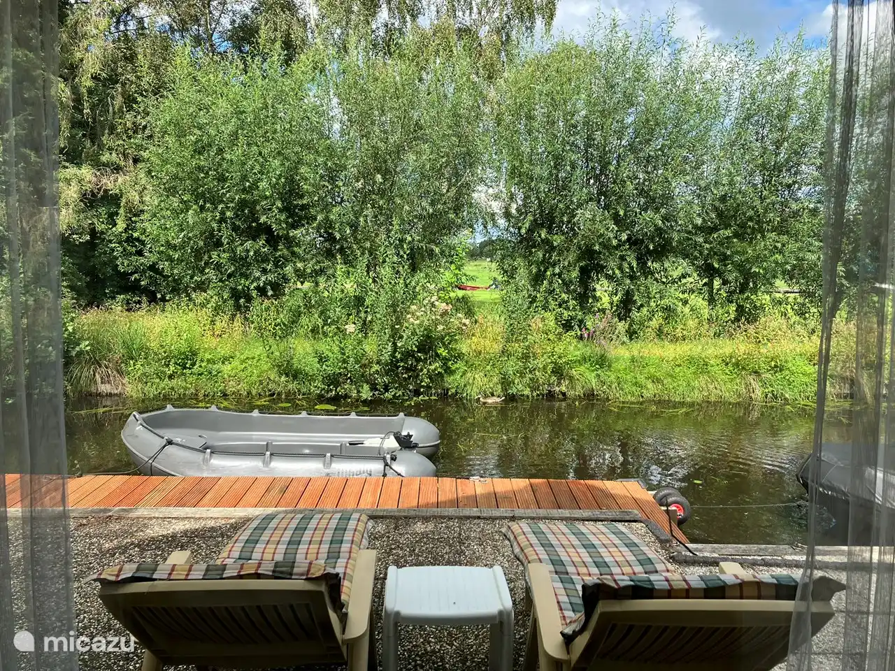 Uitzicht vanuit de woonkamer over de privé sloot waar de eendjes voorbij zwemmen en verderop achter de boompjes de Dorpsgracht waar de bootjes voorbij varen. 