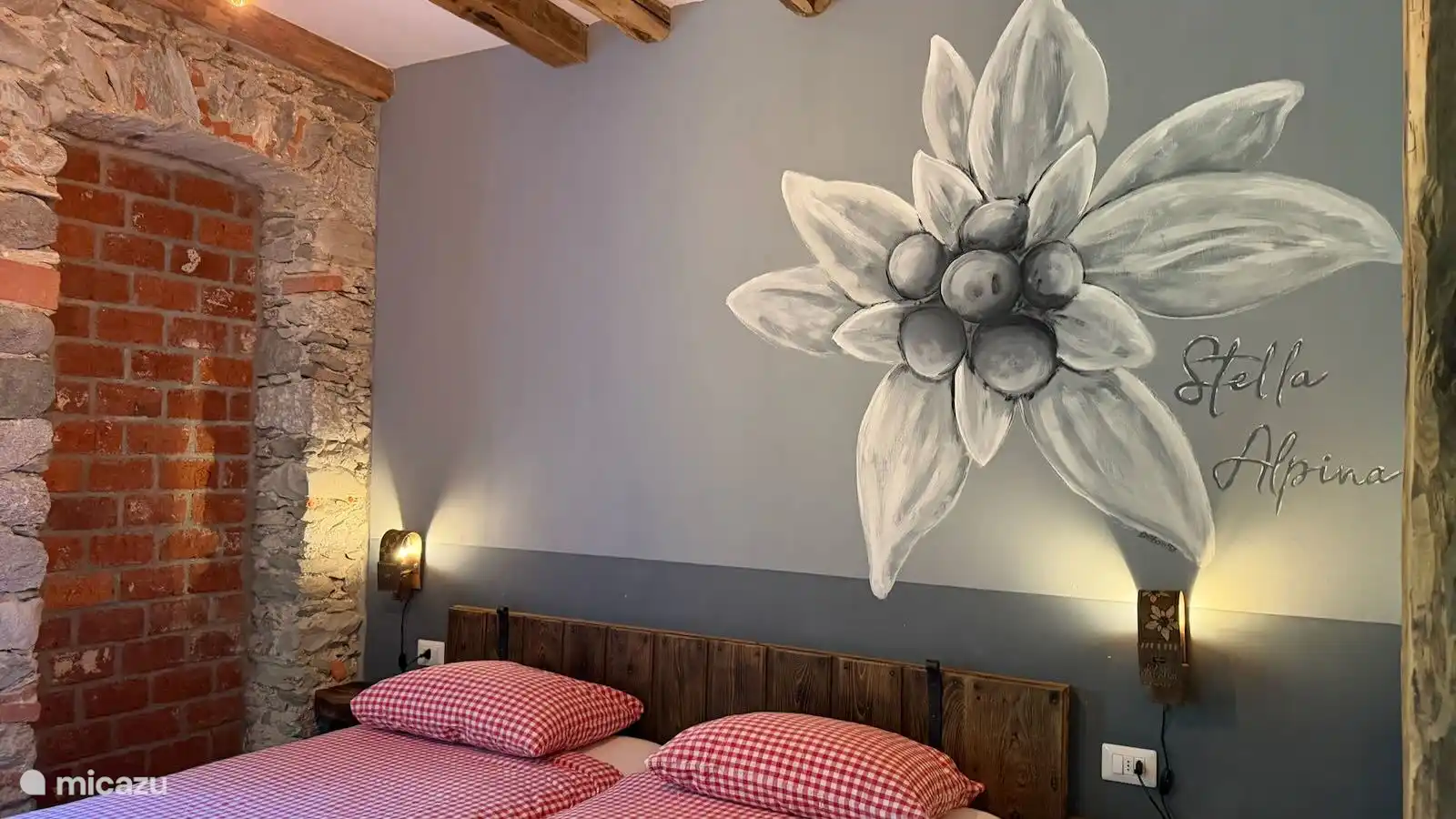 Sfeervolle slaapkamer van Appartement Stella in Valsesia, Piemonte, met comfortabele boxspringbedden, plafondventilator, authentieke natuurstenen muren en een prachtige muurschildering van een edelwei