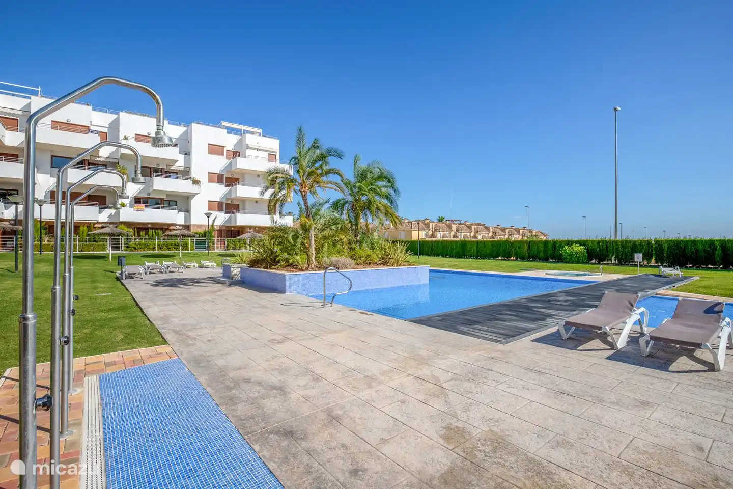 Großer Gemeinschaftspool in einem schönen Garten mit Liegestühlen und Sonnenschirmen