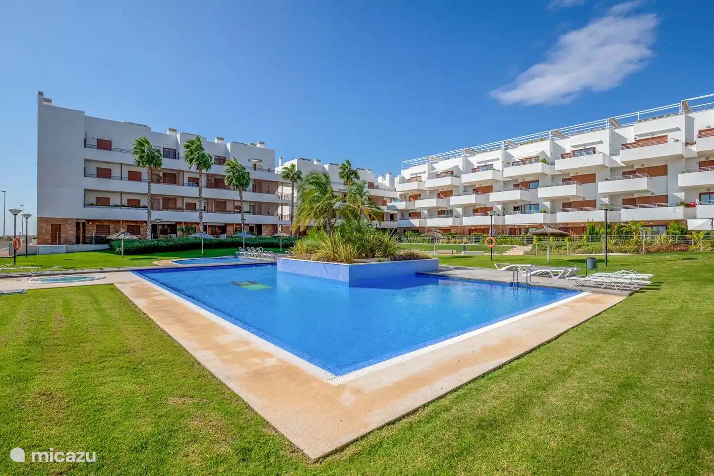 Großer Gemeinschaftspool in einem schönen Garten mit Liegestühlen und Sonnenschirmen