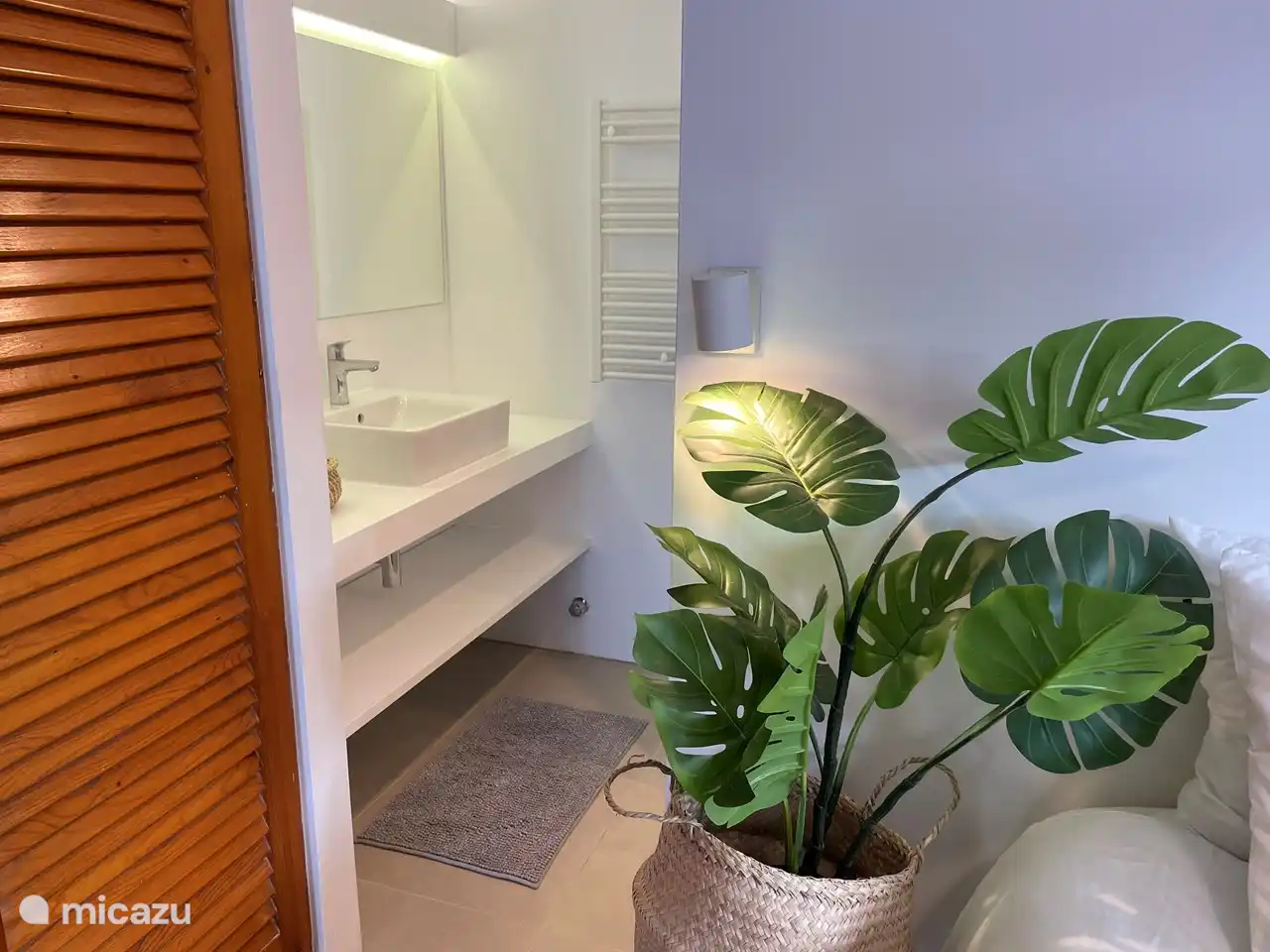 À côté de la chambre, vous avez accès à la salle de bain par une porte coulissante.  La salle de bain dispose d’un grand lavabo, d’une machine à laver, de toilettes et d’une douche spacieuse.