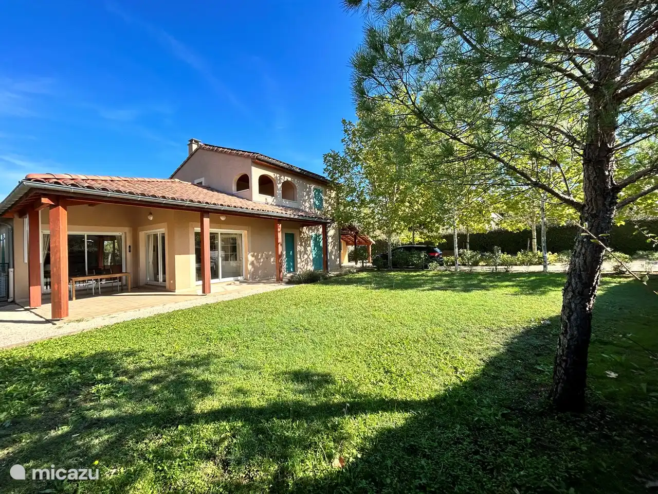 Vorgarten mit großer Rasenauffahrt für mehrere Autos und Bouleplatz und überdachten Sitzgelegenheiten.