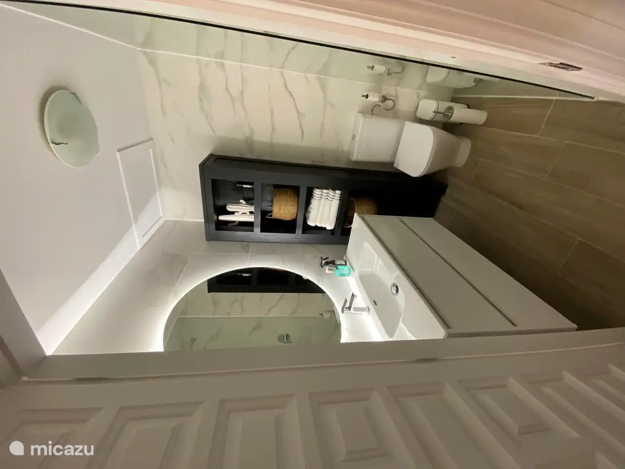 The bathroom with large sink with large round mirror and toilet.