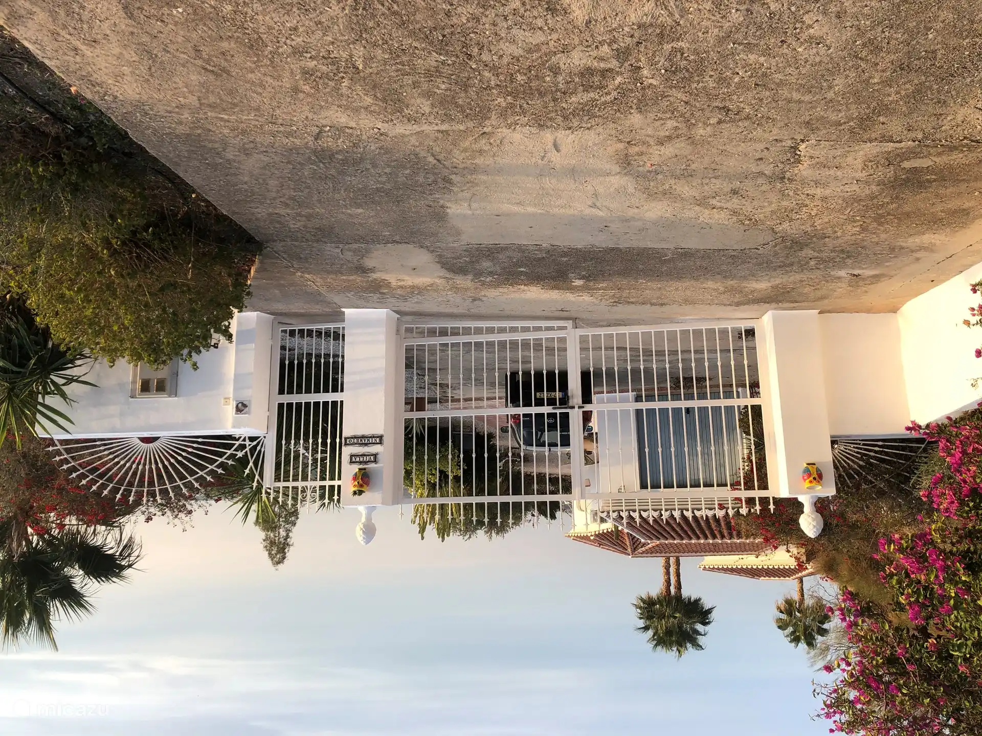 The entrance gate of Villa Nimameto with ample parking for several vehicles behind it.