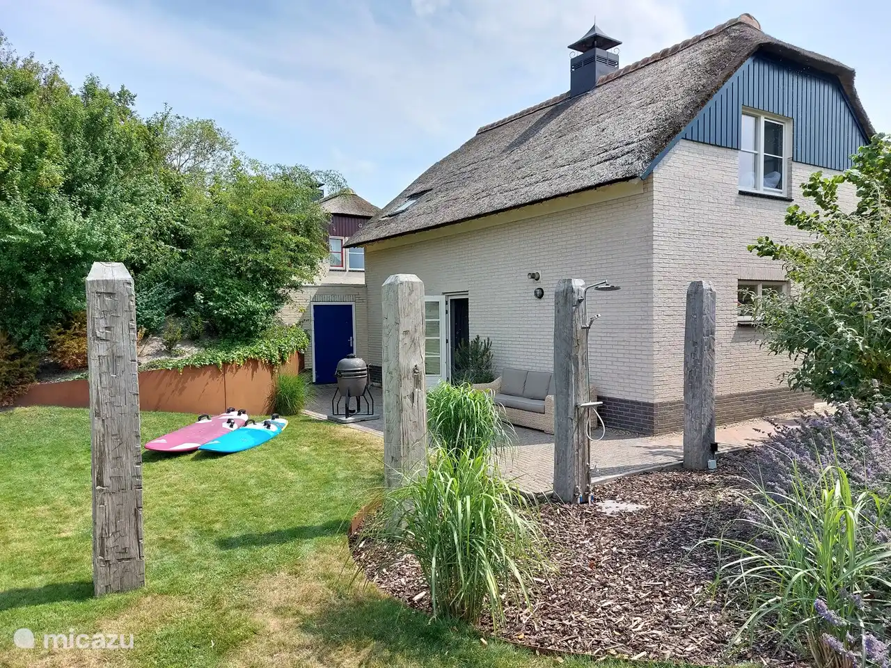 Parte trasera de la casa con patio trasero, sofá lounge, ducha caliente al aire libre y barbacoa.