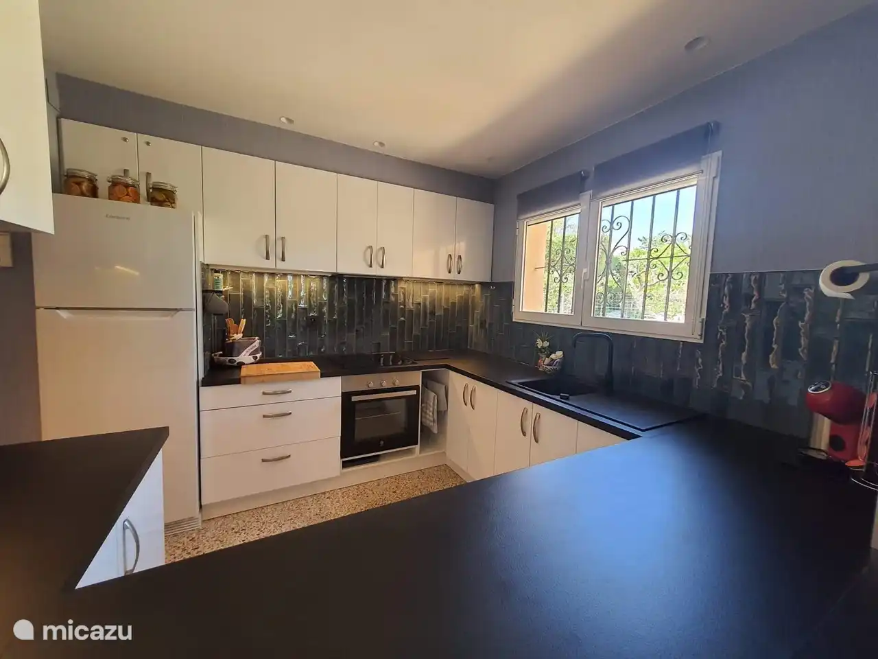 Halboffene Küche mit Cerankochfeld, Mikrowelle, Backofen, Kühl-/Gefrierschrank, Dulco-Gusto-Kaffeemaschine und Geschirrspüler.