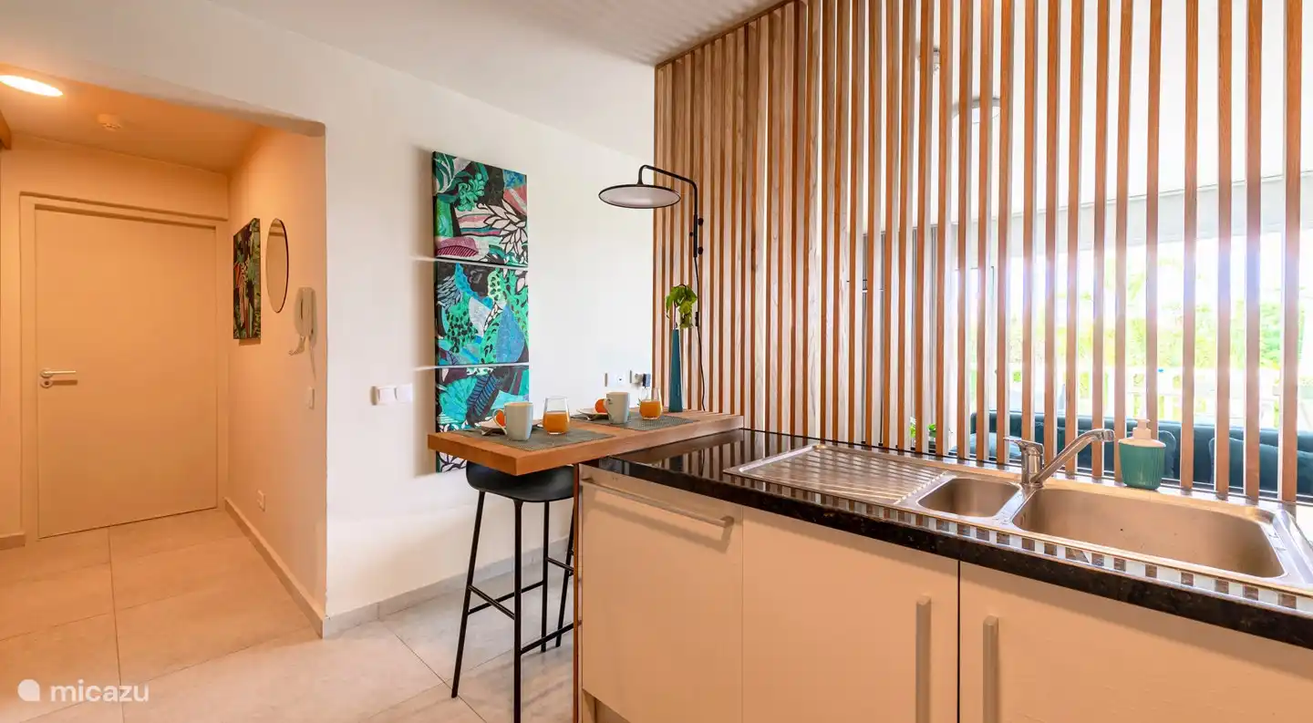 La cuisine avec vue sur le hall et le passage vers le séjour. Entre la cuisine et le salon se trouve un joli mur à lattes transparentes.