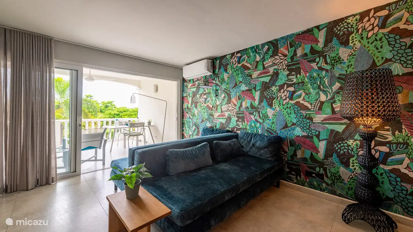 Le salon avec des canapés confortables, la climatisation, de grandes portes coulissantes donnant sur le balcon avec coin repas et salon et des voilages intermédiaires.