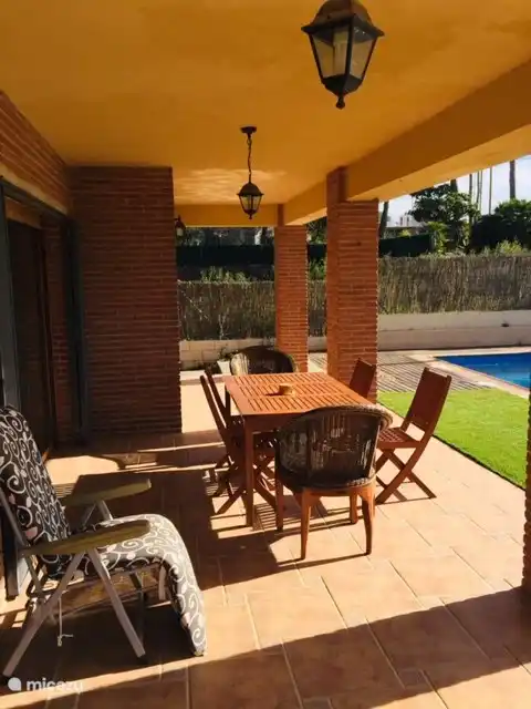 Overdekt terras, 2 tafels met stoelen en zicht op zwembad. Grote schuifraam naar de eetkamer en living.