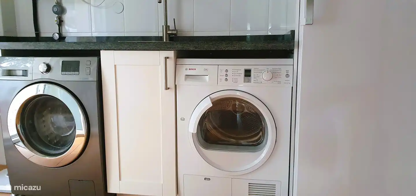 Hay un lavadero con lavadora, secadora y congelador grande.