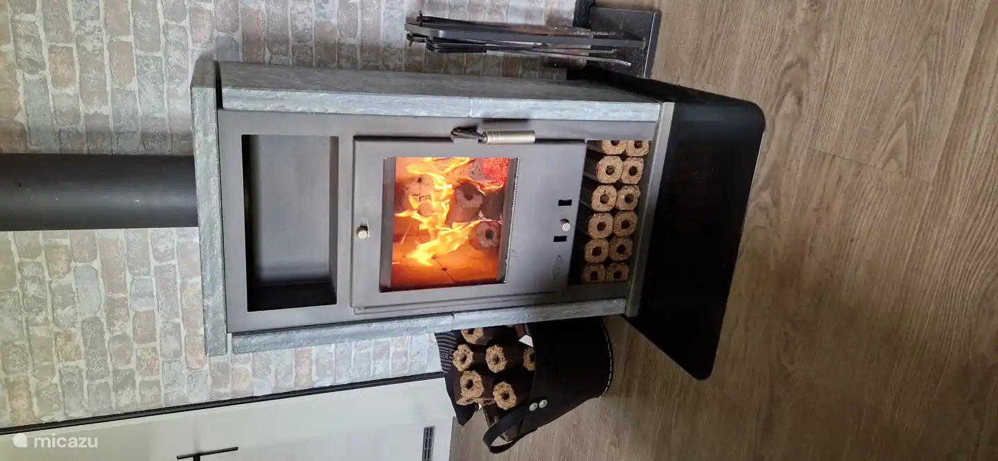 Esta robusta estufa de esteatita se encuentra en la sala de estar. Puede hacer uso gratuito de los troncos de madera prensada disponibles.