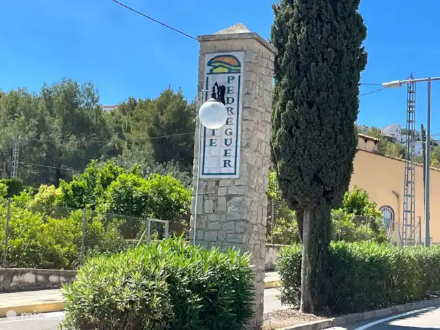 Casa Yavari en España, Costa Blanca, Pedreguer  - villa Acceso a la Urbanización Monte Pedreguer
Imponente puerta de entrada con pilares de piedra, dotada de iluminación ambiental y rodeada de exuberantes plantas. Una entrada elegante que refleja el encanto de la urbanización.