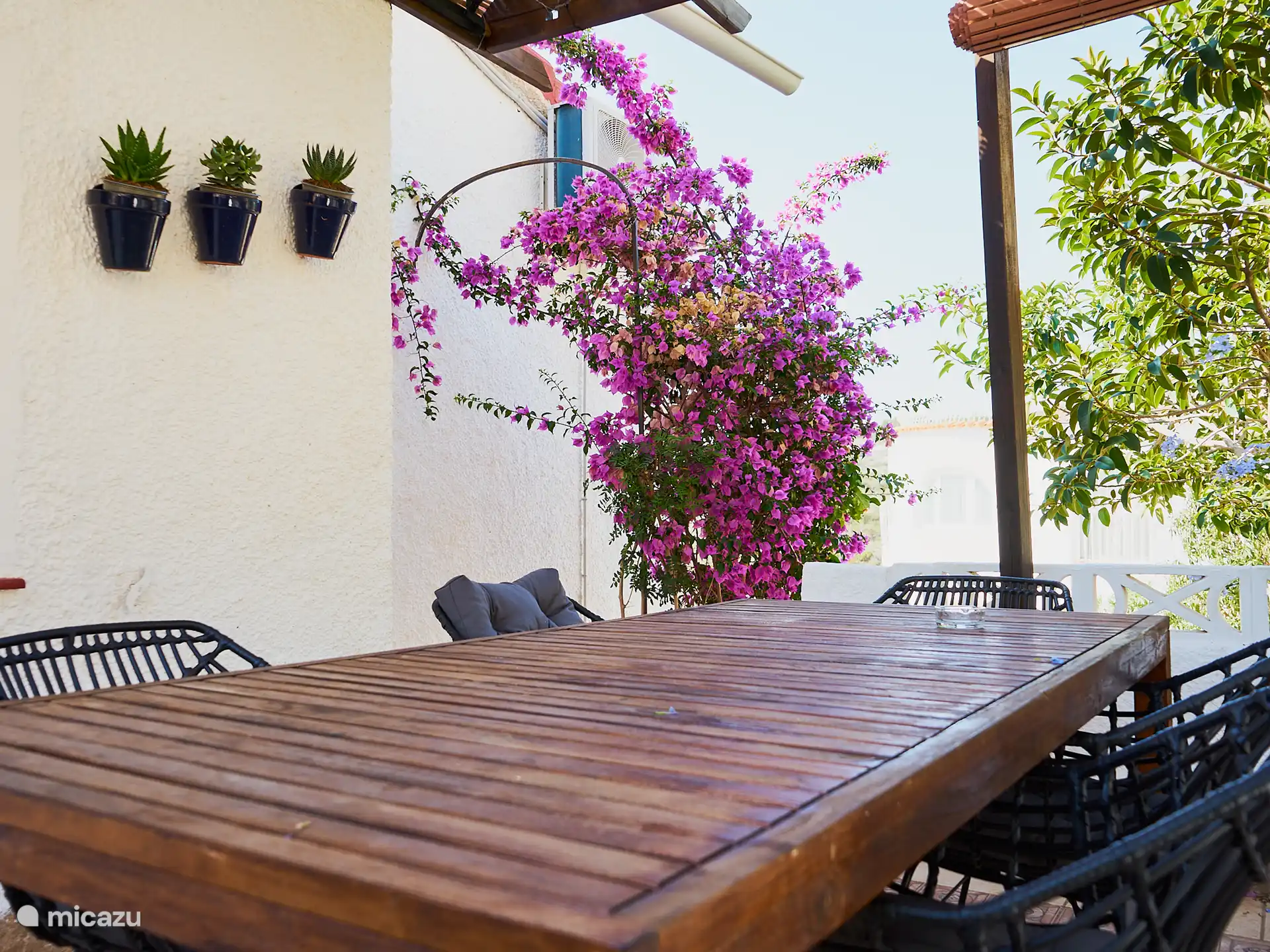 Blick von der Haustür der Casa Yavari
Von der Haustür aus blickst du auf das höhere Tor. Auf der linken Seite sehen Sie die Pergola im Ibiza-Stil mit zwei schwarzen Ibiza-Lampen, die von üppigen Blumen umgeben sind. Ebenfalls zu sehen ist der Grill, der perfekt in diesen attraktiven Außenbereich integriert ist.