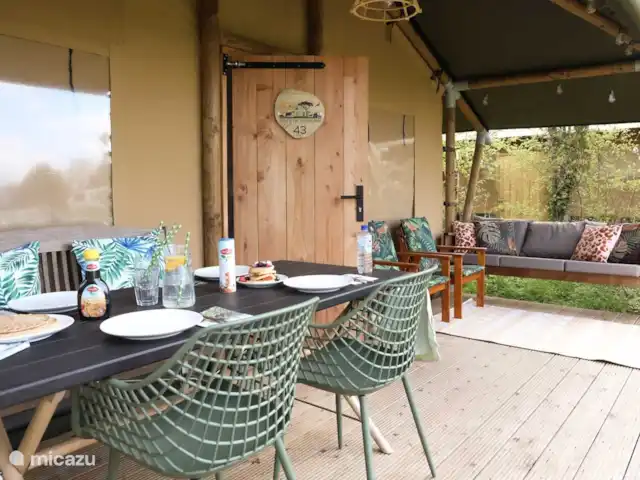 Pavillon Grutte Fiif Safari avec climatisation | Pays-Bas, Frise, Grouw - glamping / tente safari / yourte Belle véranda couverte avec cuisine extérieure, canapé de salon et ensemble de salle à manger.