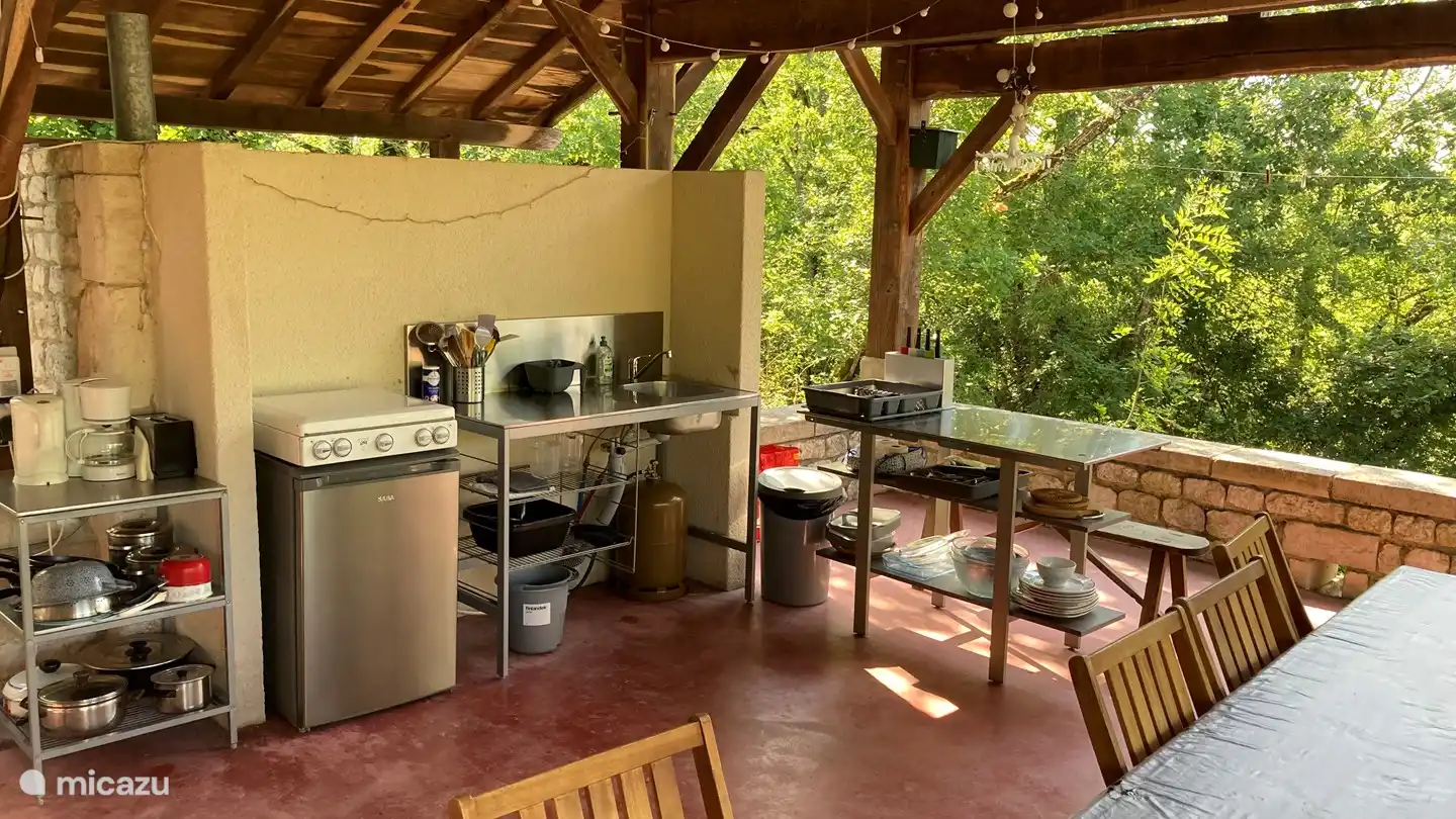 Cuisine extérieure avec cuisinière à gaz 4 feux, réfrigérateur, évier et plan de travail.