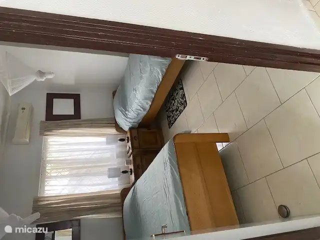 two oak single beds with bedside tables and TV on the wall.