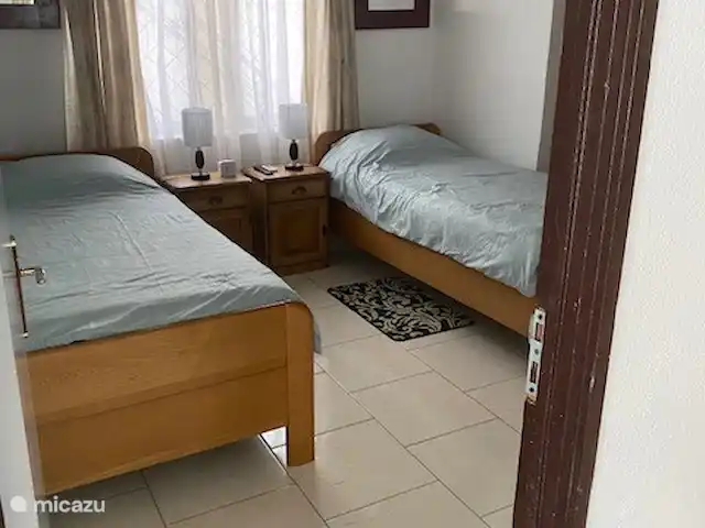Location de Vacances Suriname, Paramaribo, Paramaribo, maison de vacances - Mendes House Appartement au rez-de-chaussée deux lits simples en chêne avec tables de chevet et TV au mur.
