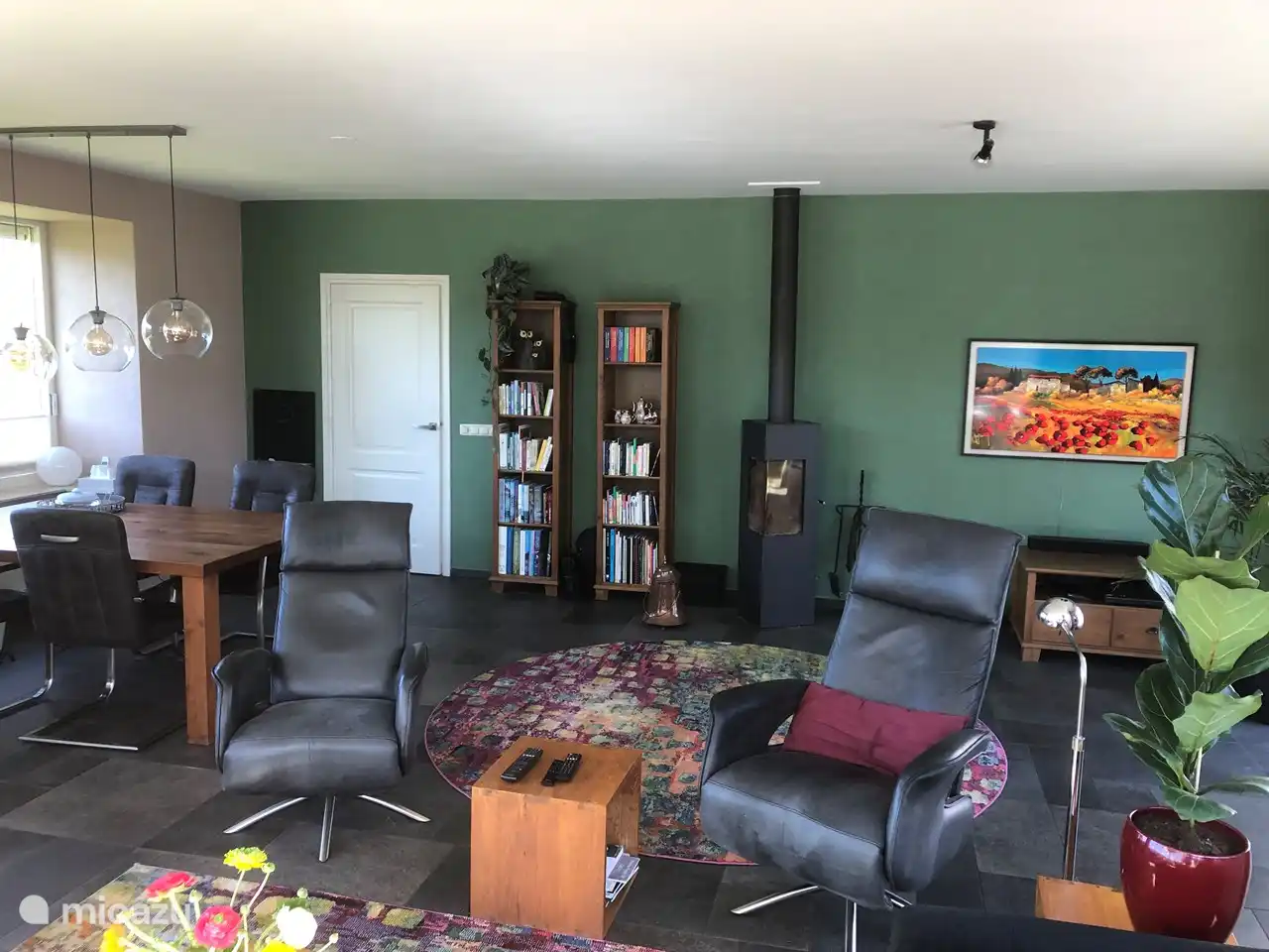 Wohnzimmer mit großem Esstisch und Holzofen. Die Sessel können zum Fernseher gedreht werden (Gemälde).