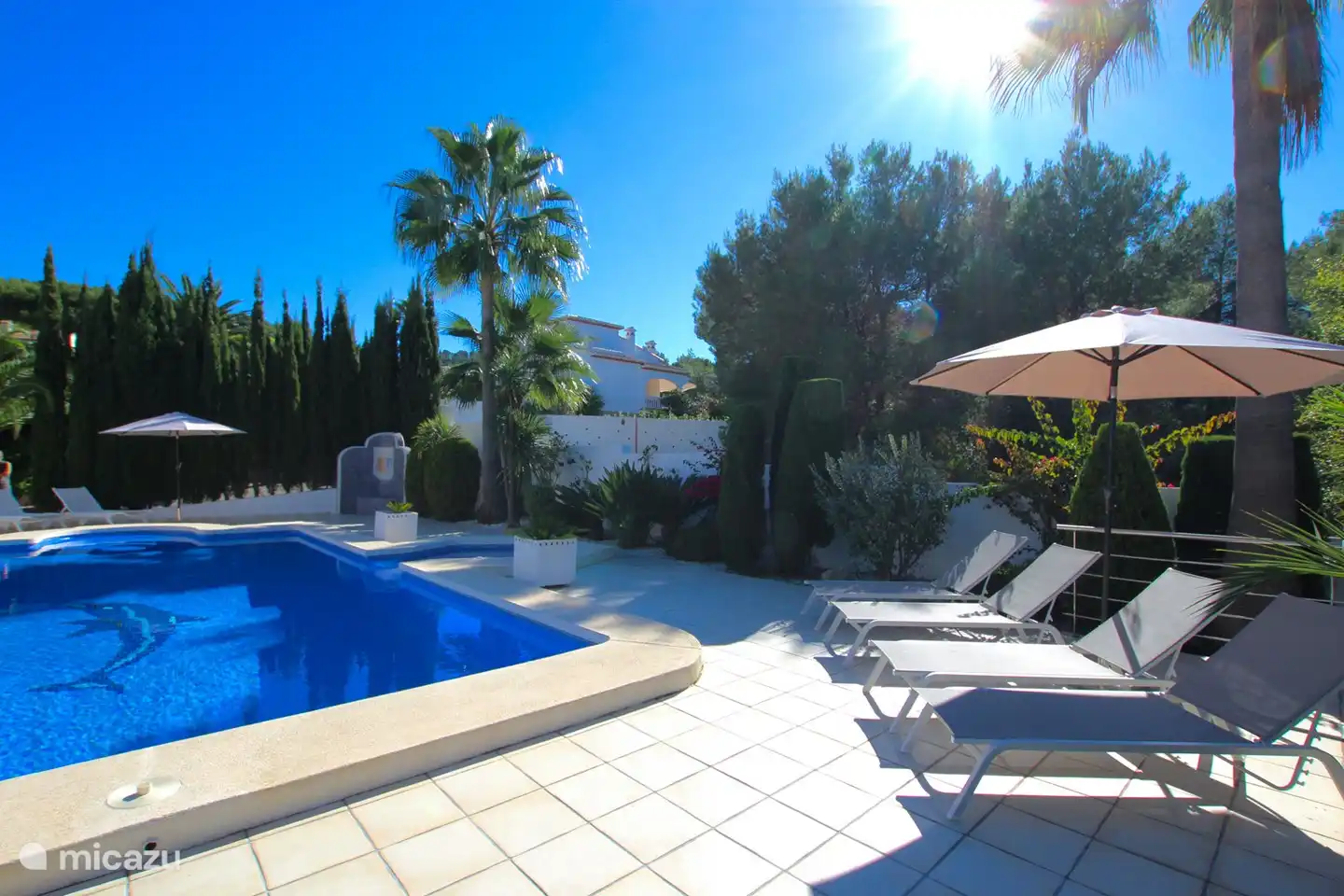 Gartenblick mit Außendusche, Sonnenliegen und Sonnenschirmen