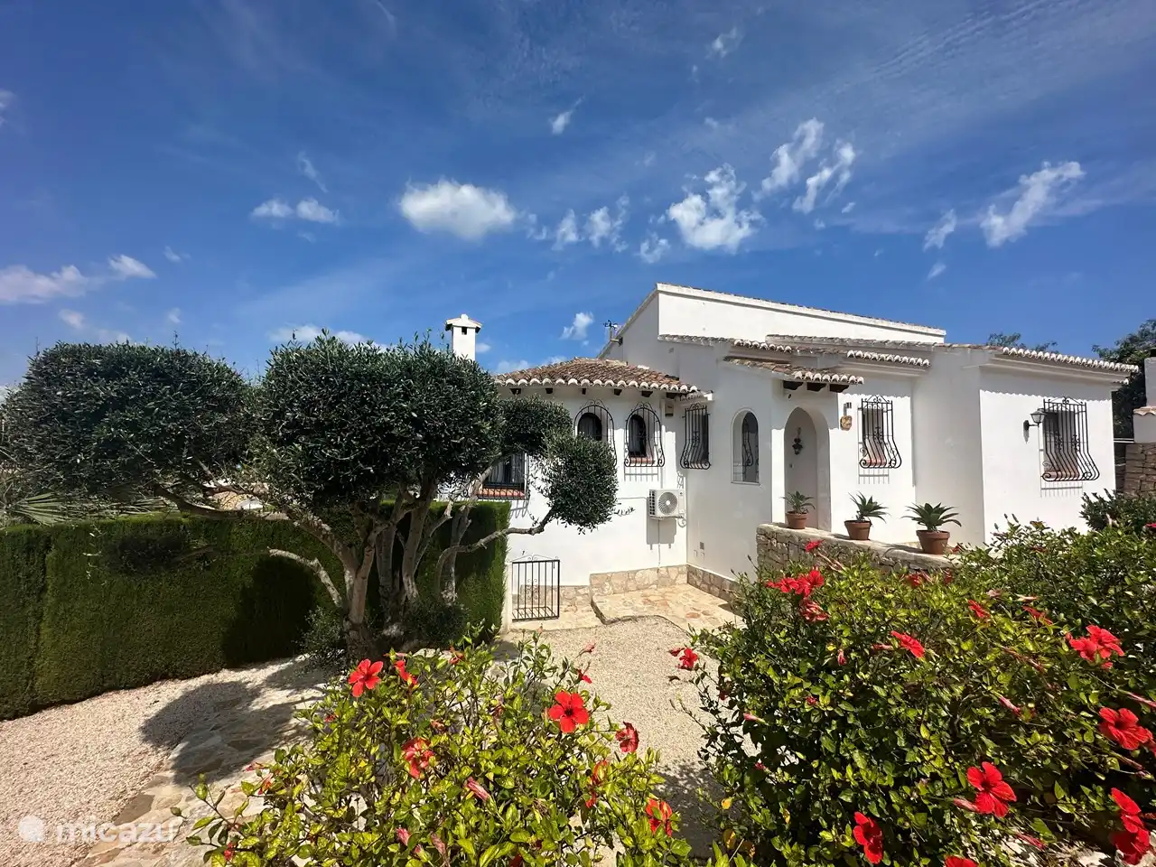Die Vorderseite des Hauses mit Vorgarten und Carport. Links und rechts gelangt man am Haus vorbei zum Garten mit Swimmingpool und Poolbar, aber auch zur darunter liegenden Wohnung.