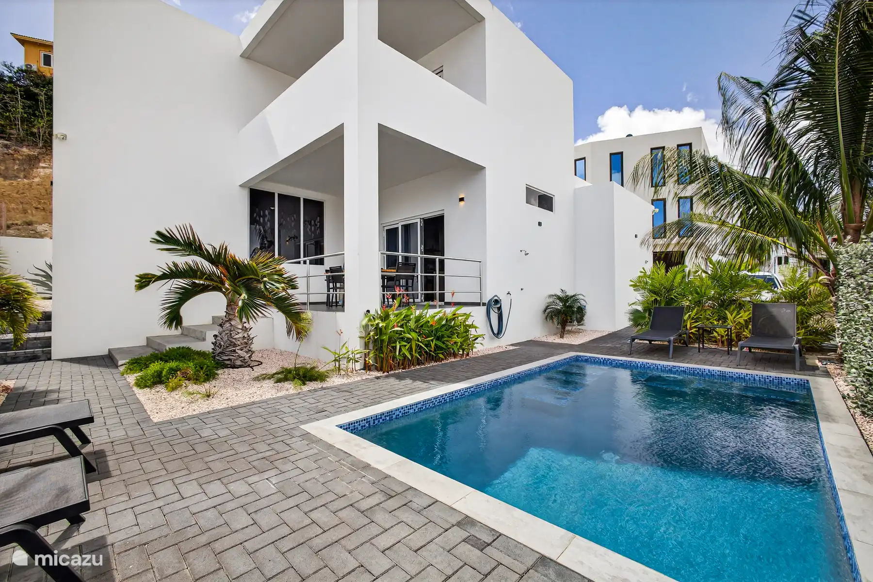 Moderne villa met privézwembad, omringd door palmen en een zonnig terras.