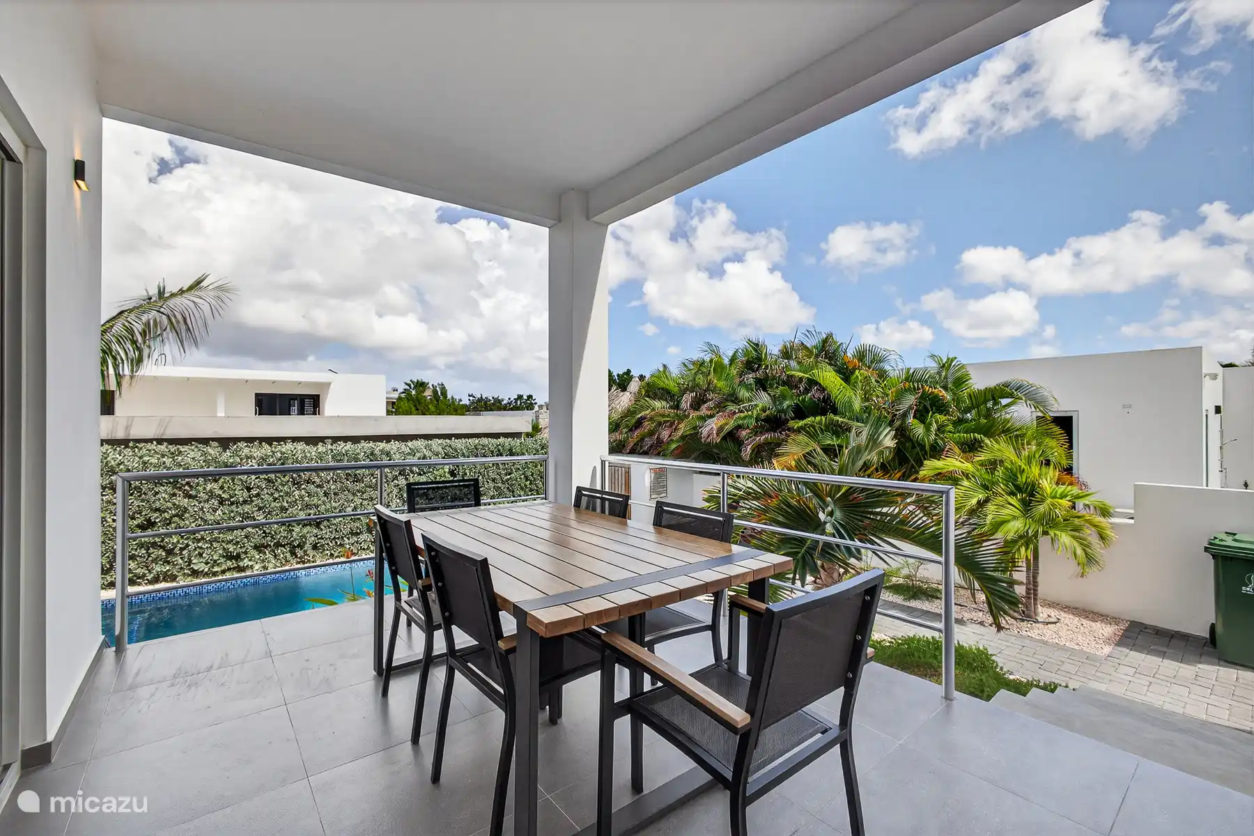 Overdekt terras met eettafel en uitzicht op de tuin en het zwembad.