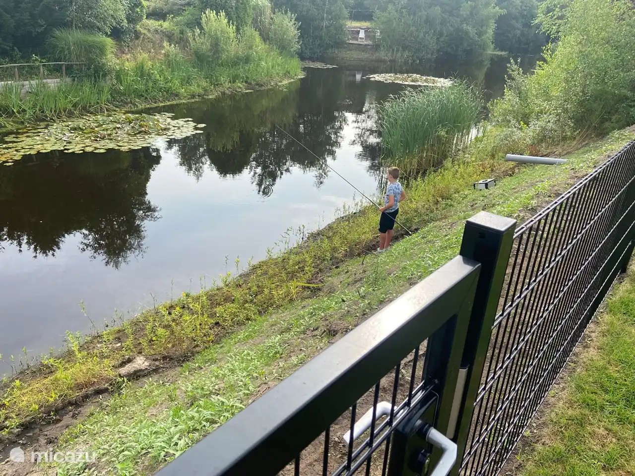 Visvijver achter hekwerk met toegangspoort die door een volwassenen wordt beheerd