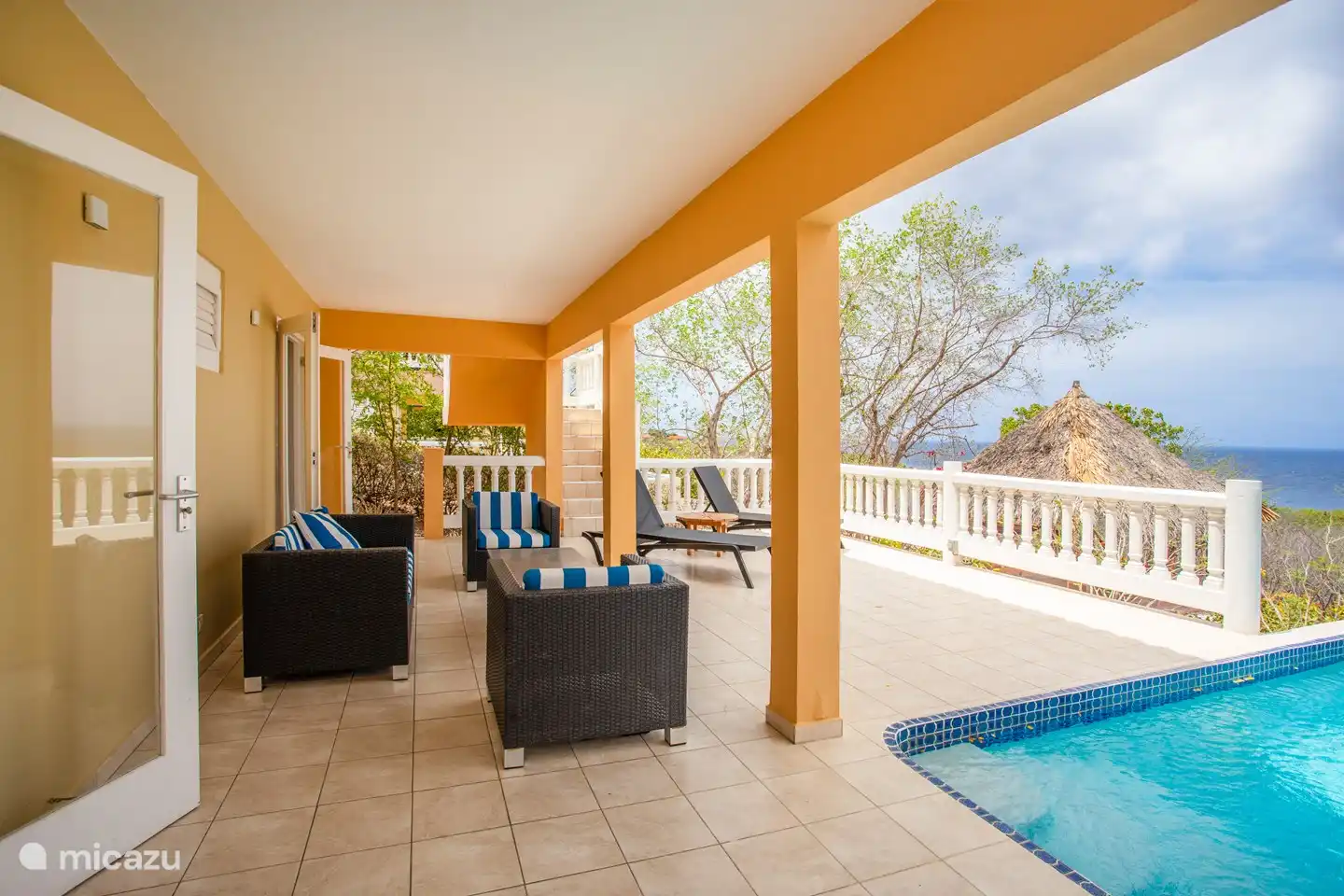 Shaded pool deck with comfortable loungers and sofas and the patio doors of the downstairs bedrooms.