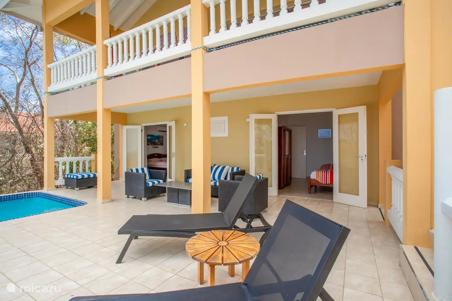 Shaded pool deck with comfortable loungers and sofas and the patio doors of the downstairs bedrooms.