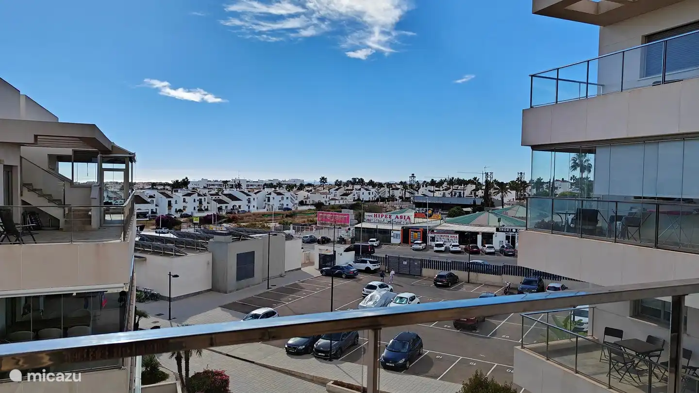uitzicht rechts vanaf balkon met zicht op parkeerplaats en lokaal winkelcentrum met supermarkt.