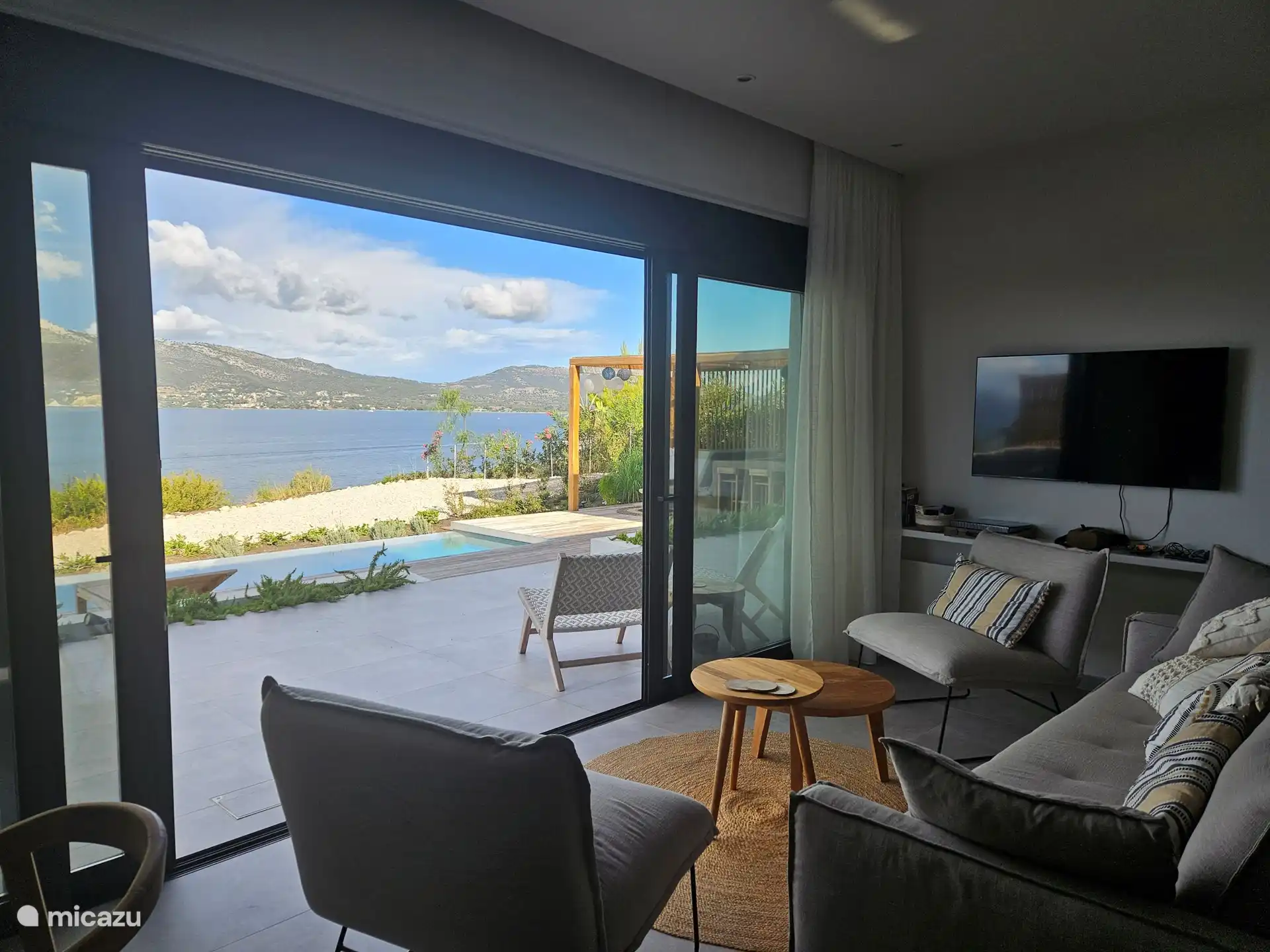 Blick vom Wohnzimmer auf den Pool, den Loungebereich und die Bucht