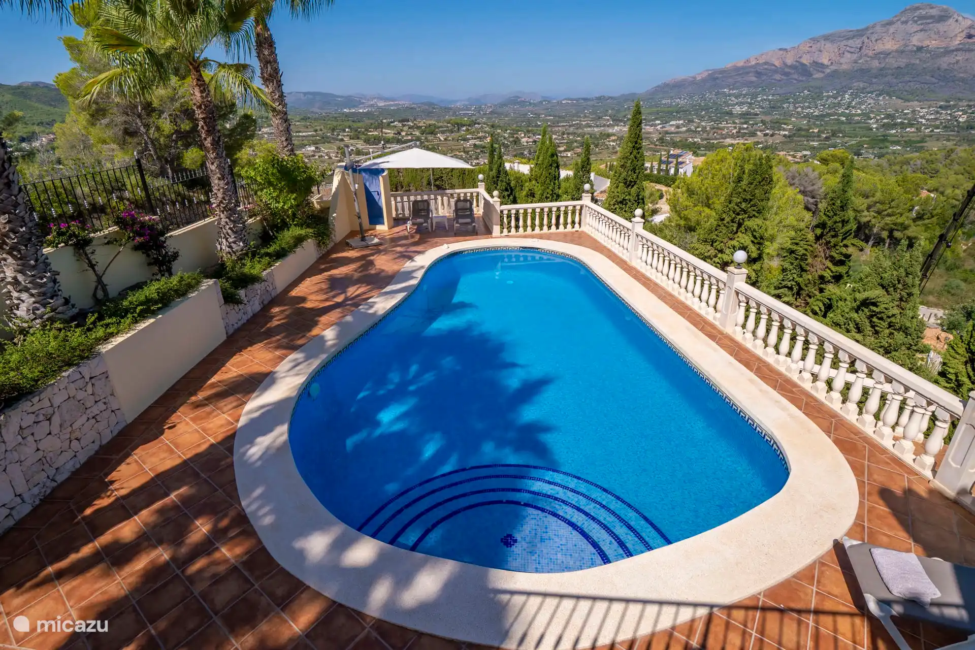 Large kidney-shaped swimming pool with wide stairs. Sunbeds and parasol