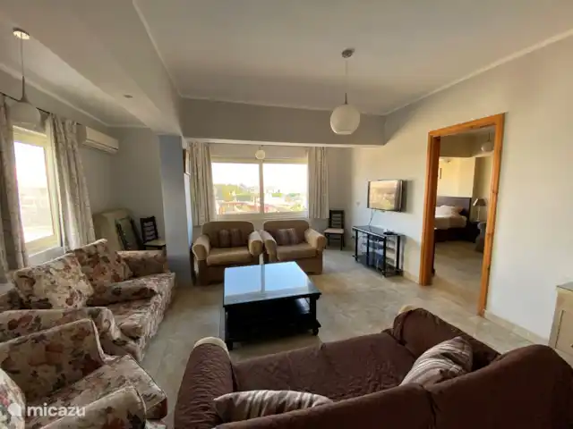 Voir Villa Appartements, app 6pers. | Égypte, Mer Rouge , Hurghada - appartement Séjour avec vue mer et piscine.
Il y a 2 canapés confortables et 3 fauteuils séparés avec une grande table basse.
Un téléviseur à écran plat Samsung est accroché au mur.