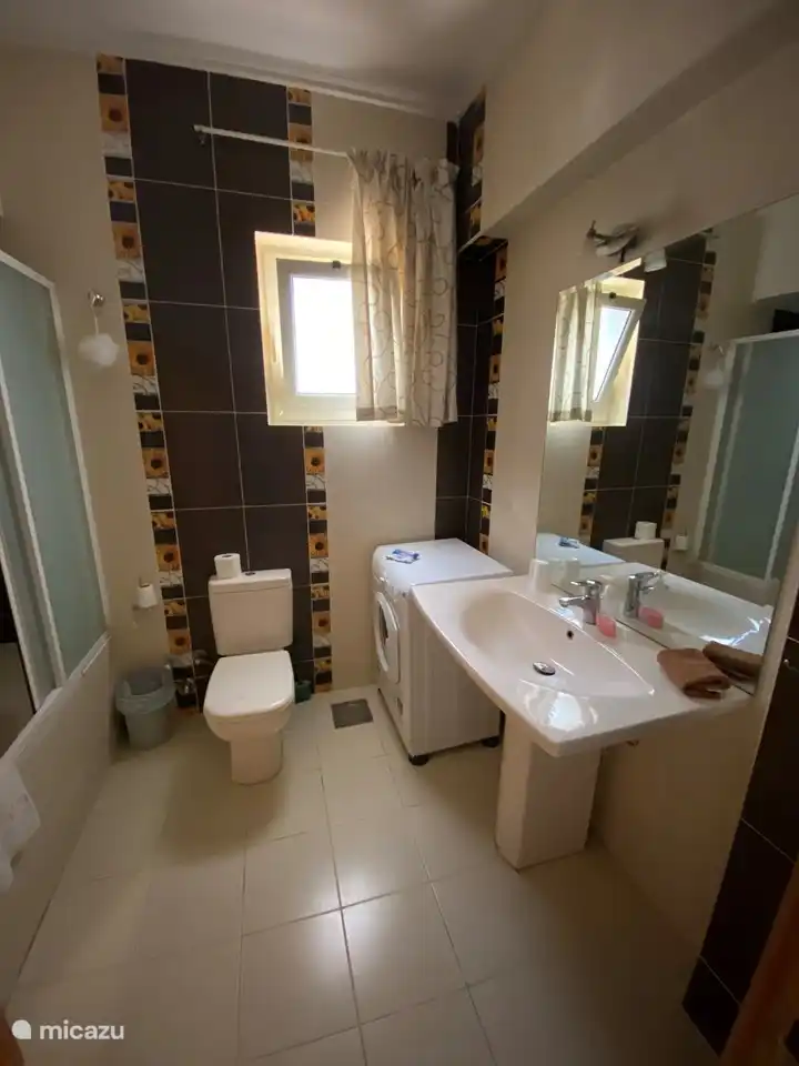 Spacious bathroom with bath/shower with shower screens, sink, toilet and washing machine.