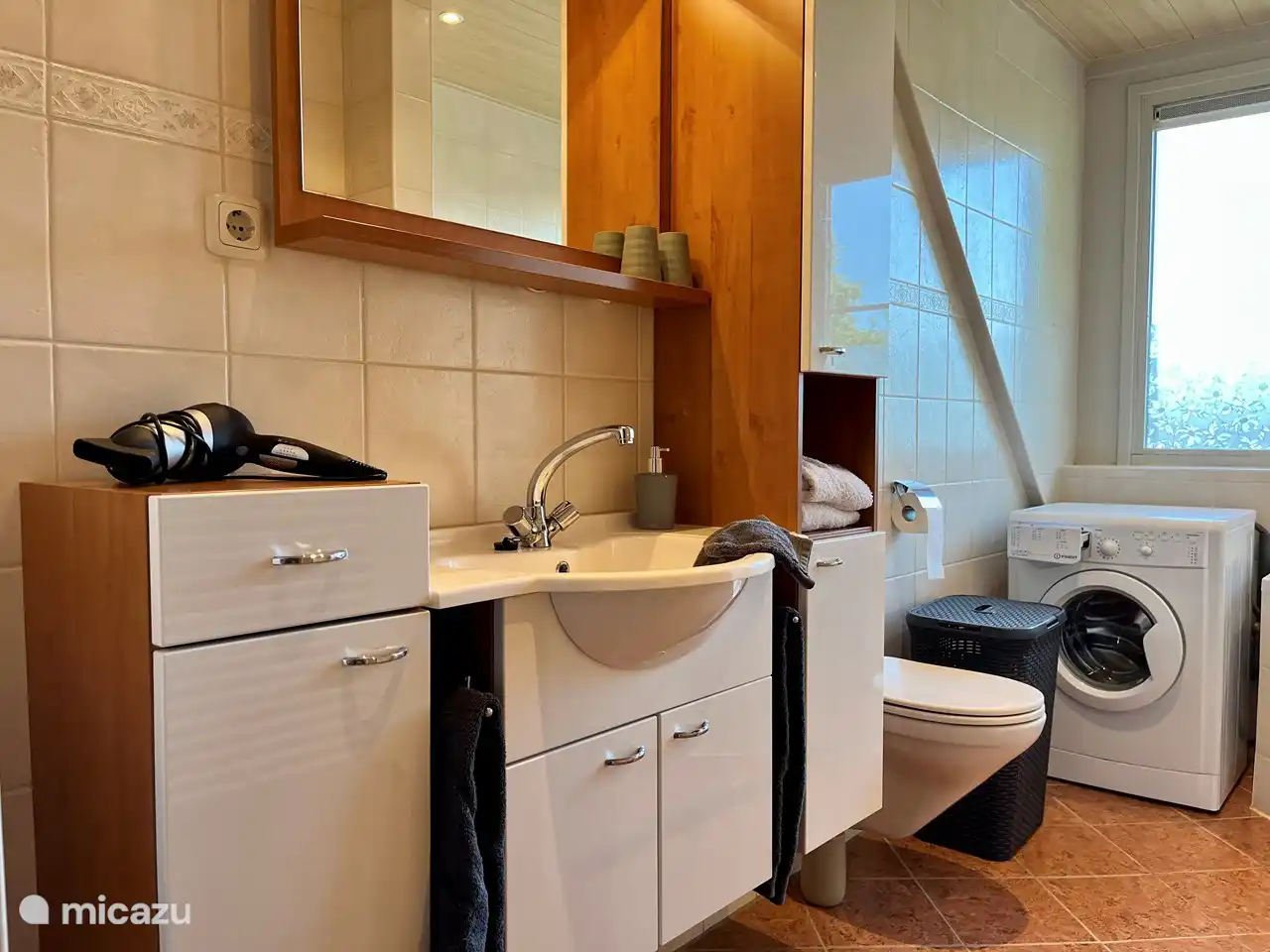 Badezimmer mit Badewanne, ebenerdiger Dusche, Haartrockner, Waschmaschine und viel Stauraum.