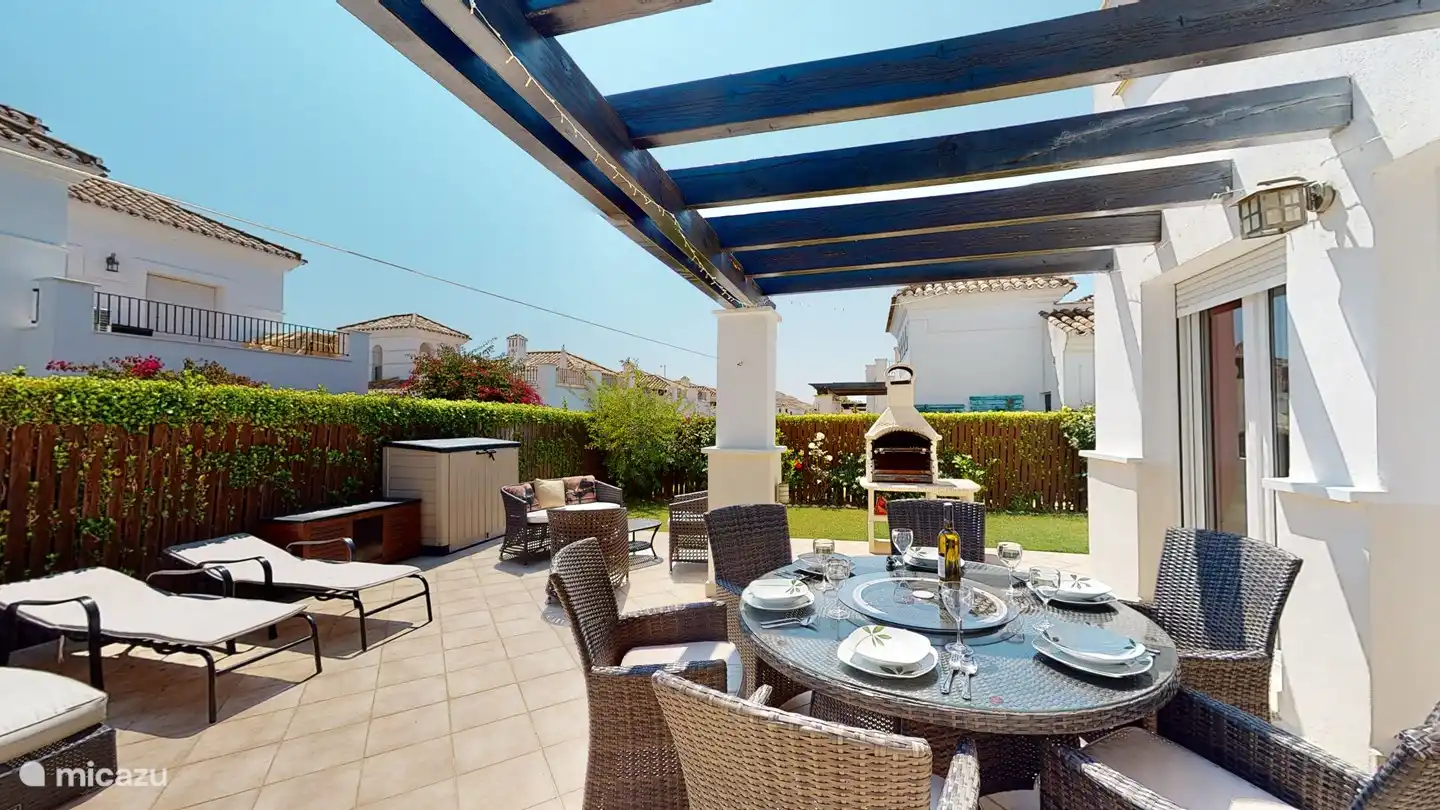 Terrasse derrière le salon avec 6 bains de soleil avec coussins, 6 chaises de salle à manger, table ronde avec plateau en verre, au milieu un plateau tournant en verre. barbecue. 2 bacs de jardin pour ranger les coussins de transat et de chaise.