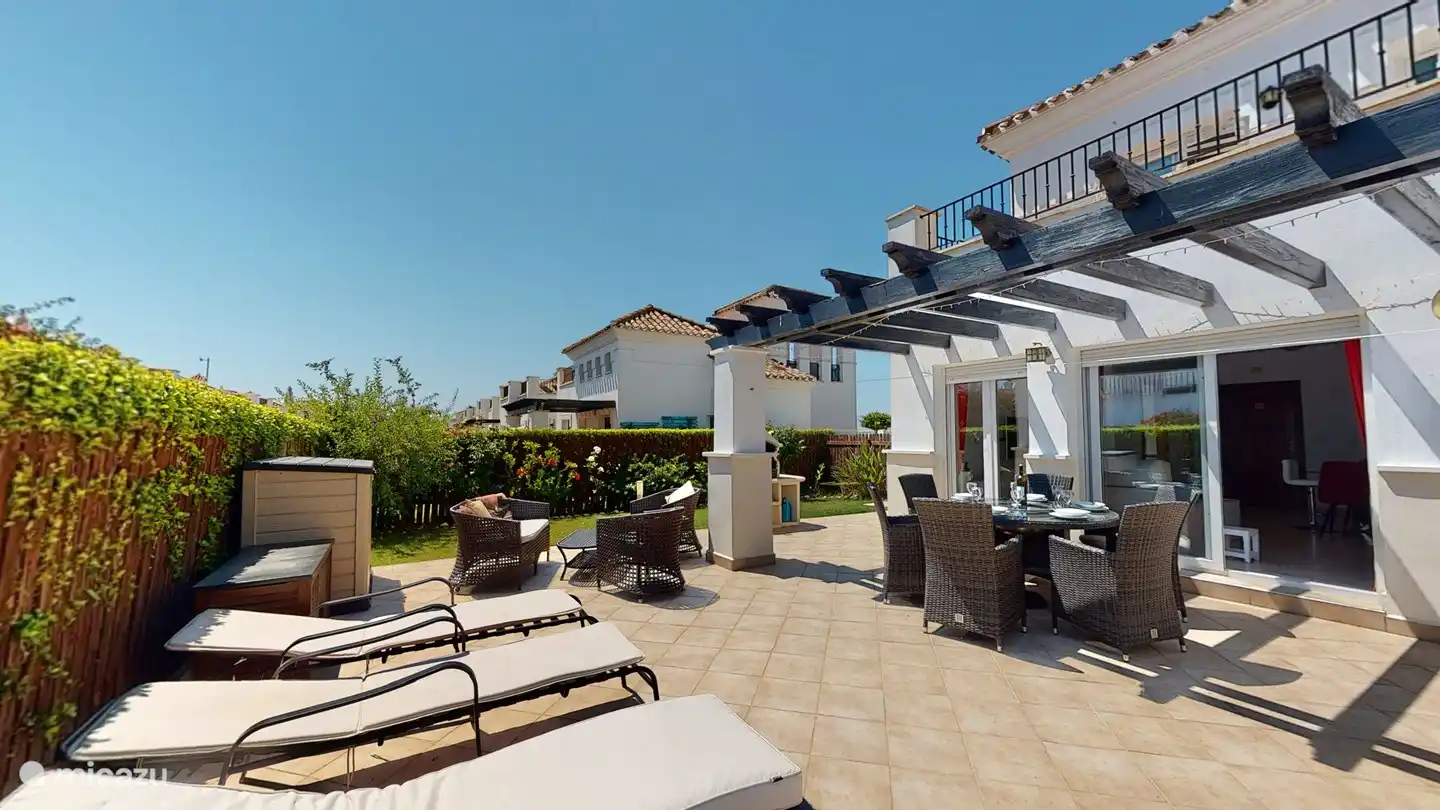 Terrasse derrière le salon avec 6 bains de soleil avec coussins, 6 chaises de salle à manger, table ronde avec plateau en verre, au milieu un plateau tournant en verre. barbecue. 2 bacs de jardin pour ranger les coussins de transat et de chaise.