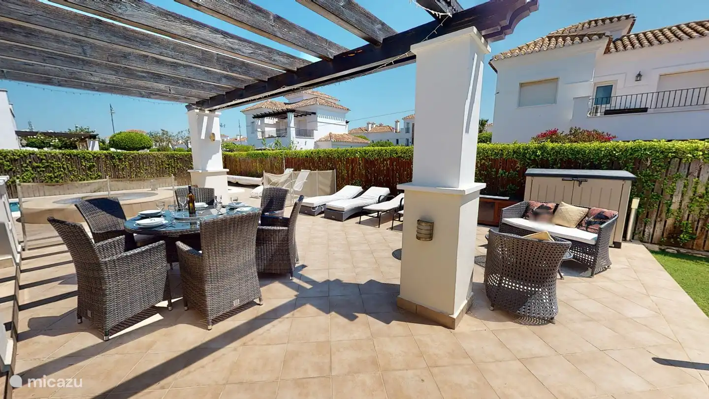 Terrasse derrière le salon avec 6 bains de soleil avec coussins, 6 chaises de salle à manger, table ronde avec plateau en verre, au milieu un plateau tournant en verre. barbecue. 2 bacs de jardin pour ranger les coussins de transat et de chaise.