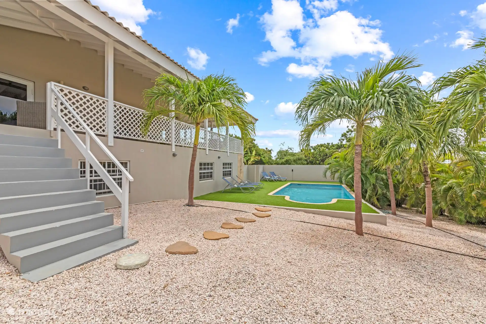 Via de trap van het terras komt u in de groene tuin met groot zwembad. Hier kunt u heerlijk ontspannen, een verfrissende duik nemen of genieten van de rust en ruimte om u heen. De tuin is omringd door weelderig groen en biedt voldoende privacy, zodat u ongestoord kunt genieten van uw verblijf.
