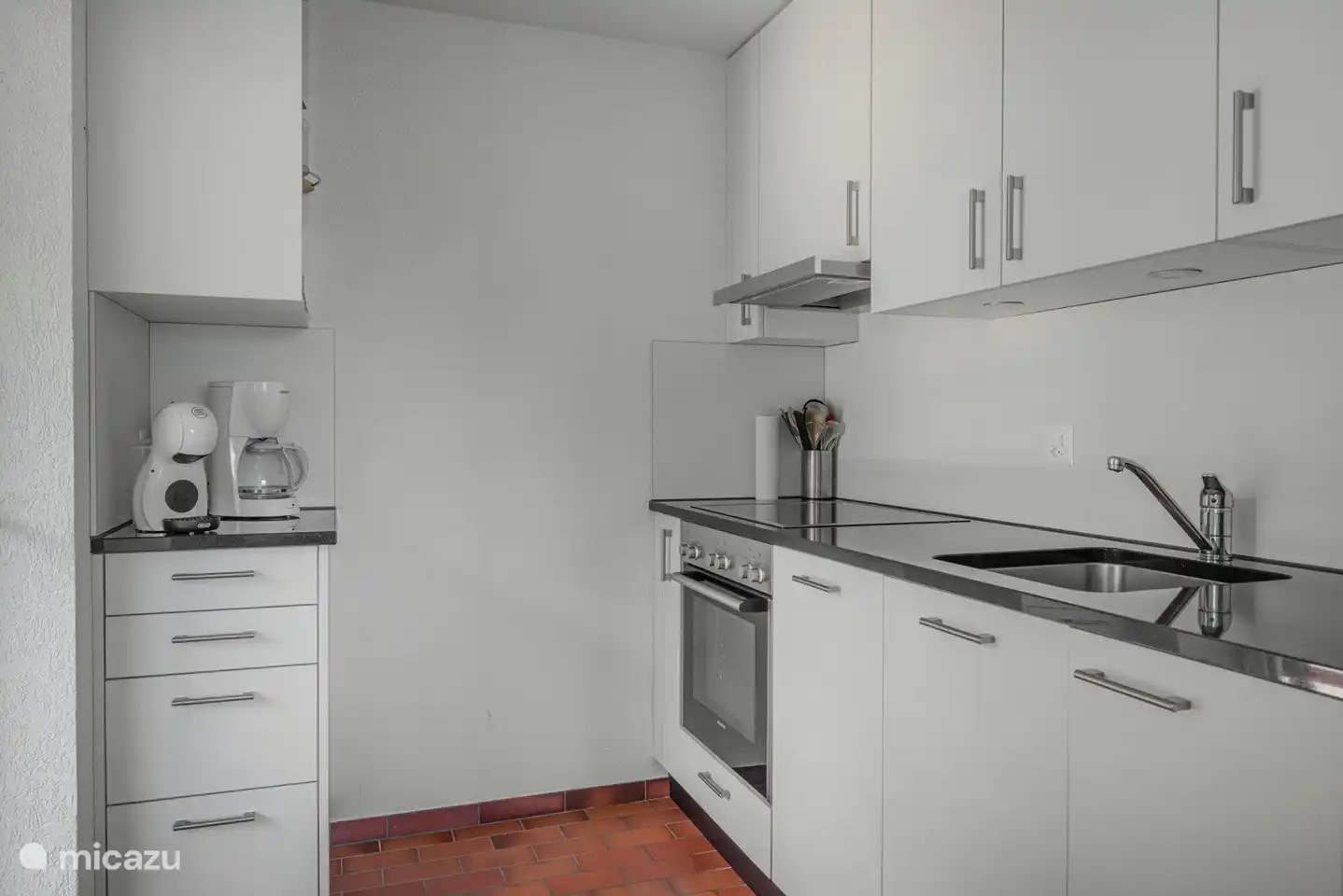 Une cuisine partiellement ouverte (neuve) avec une porte extérieure donnant sur la terrasse latérale.